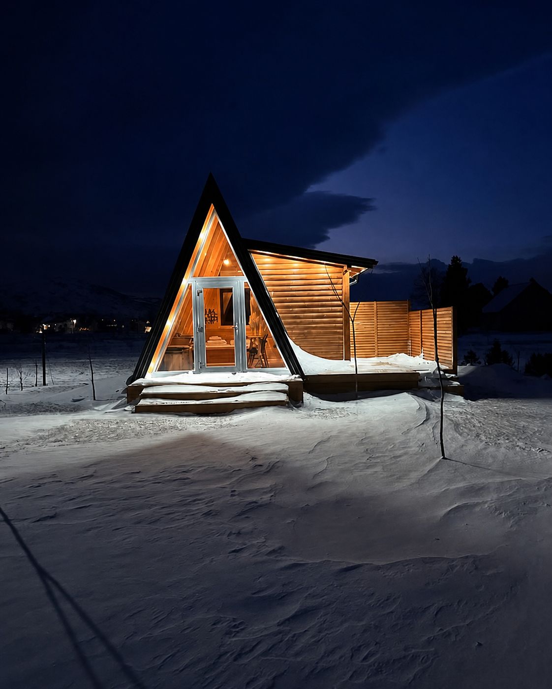 Illuminated A-frame chalet surrounded by deep snow at night